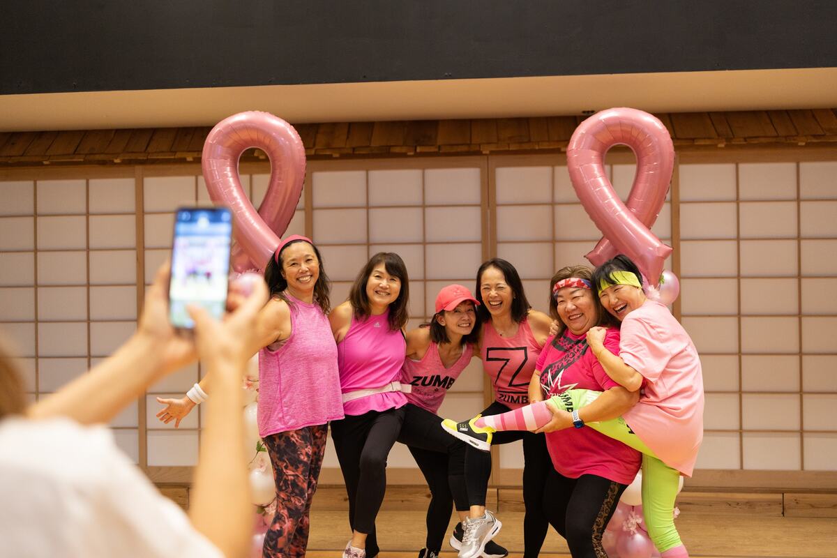 A group posing for a phone photo beside two giant pink ribbon balloons