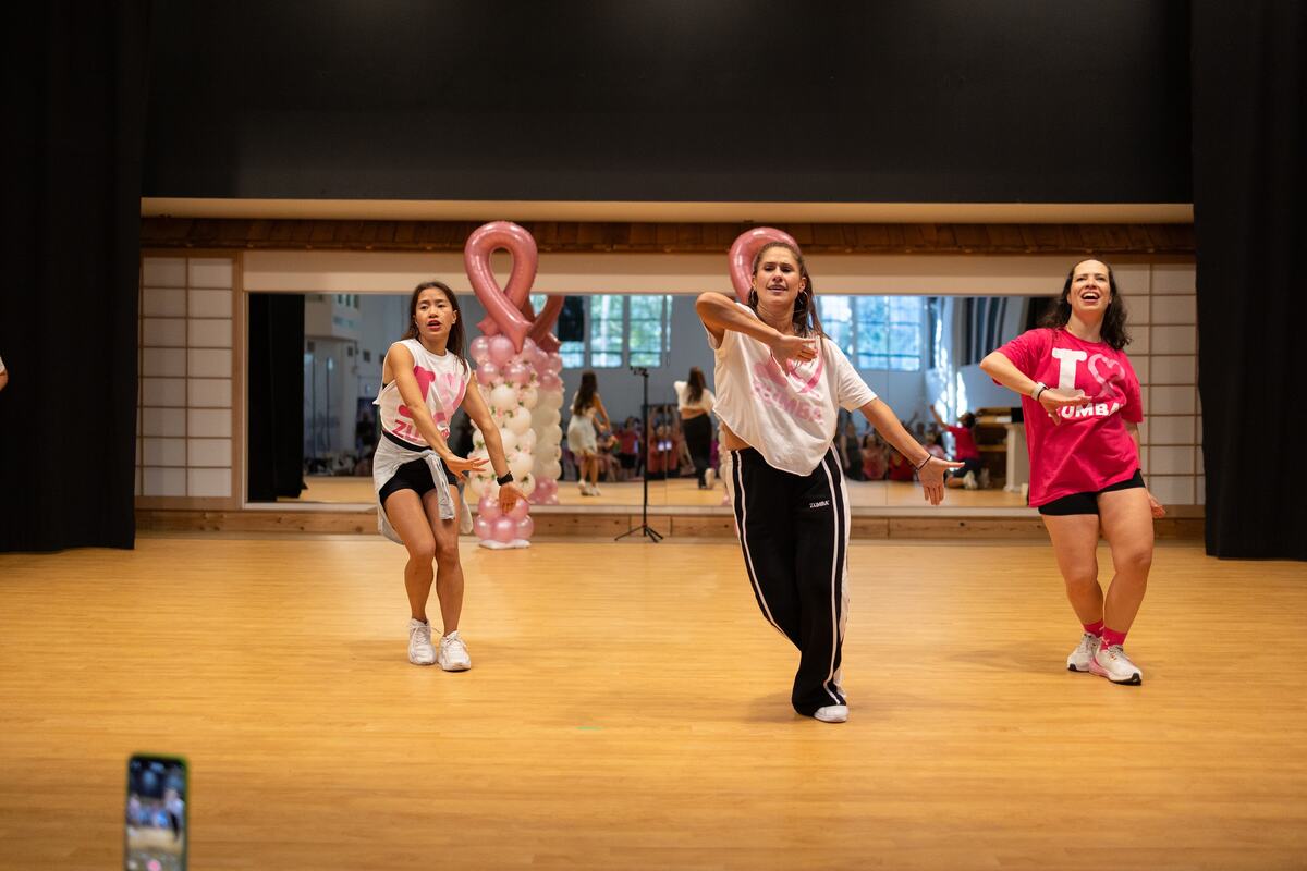 Three instructors leading a routine in front of pink ribbon balloons